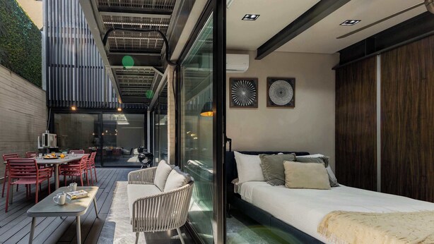 A modern interior with a glass wall, a sofa, a dining area with red chairs, and a ceiling with exposed beams.