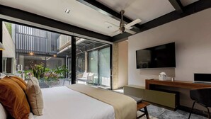 A modern hotel room with a large bed, a desk, a flat-screen TV, and a balcony with plants.
