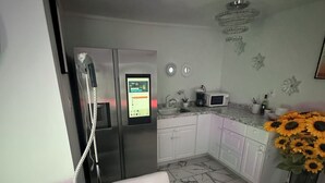 Eine moderne Küche mit Einbaukühlschrank, Mikrowelle und Spüle. Im Vordergrund steht ein weißes Sofa und auf der Arbeitsfläche steht eine Vase mit Sonnenblumen.