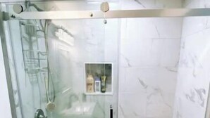 Un baño con ducha de vidrio, inodoro y un pequeño estante con artículos de aseo.