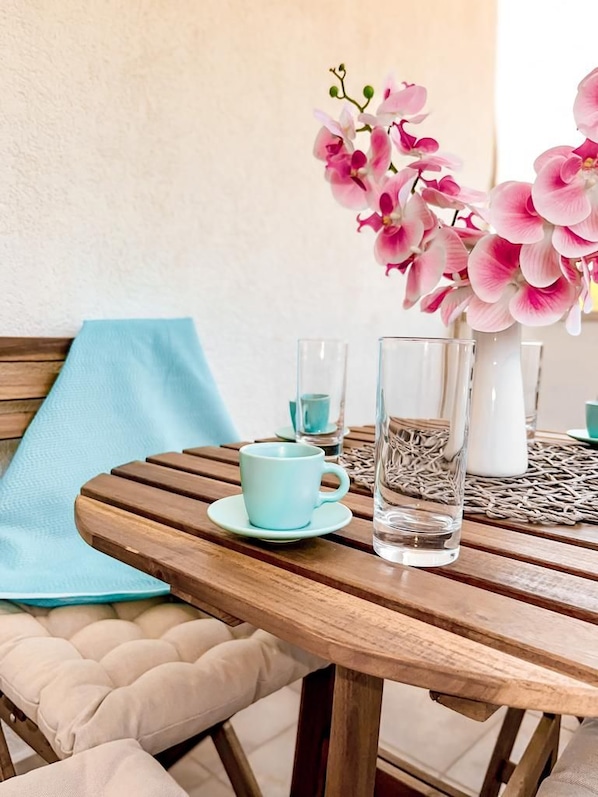 A wooden table with a clear glass, a blue cup, and a vase with pink flowers.