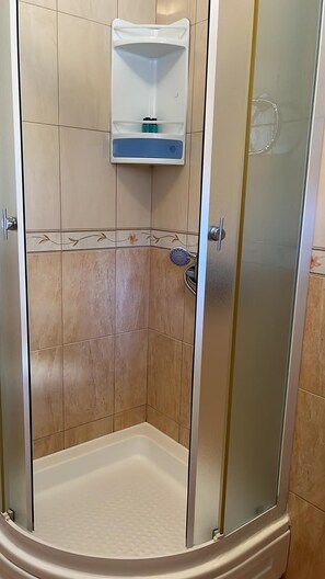 A shower enclosure with a glass door, a white shelf above the shower, and a tiled wall. - Central Apartment Bol (Bol)