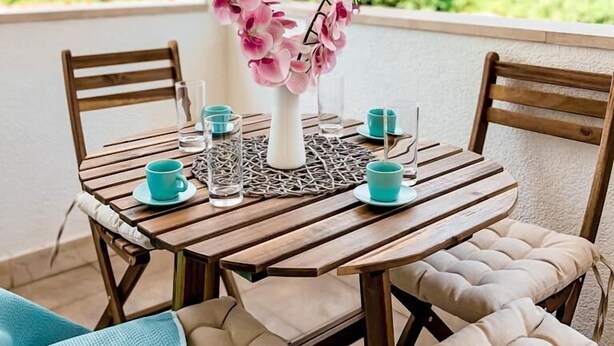 A round wooden table with a white vase of pink flowers, surrounded by four chairs with beige cushions. - Central Apartment Bol (Bol)