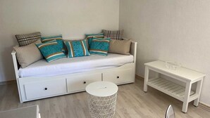 A white sofa with multiple cushions, a small round side table, and a white side table with a geometric object on top. - Central Apartment Bol (Bol)