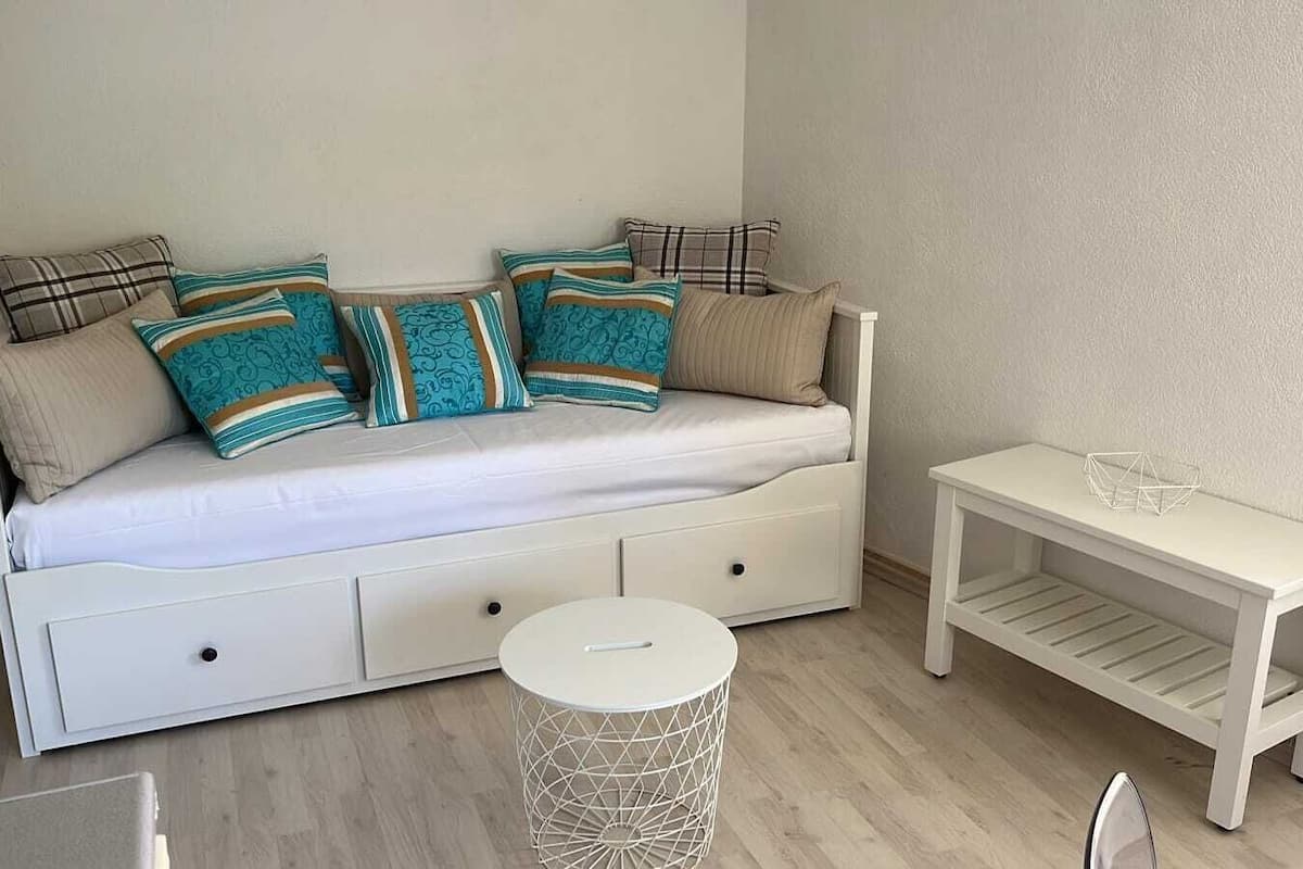 A white sofa with multiple cushions, a small round side table, and a white side table with a geometric object on top.