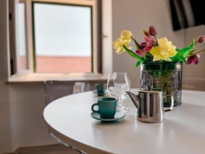 A round table with a teal cup and saucer, a glass pitcher, and a vase with yellow and pink flowers. - Central Apartment Bol (Bol)