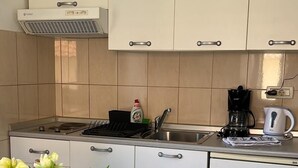 A modern kitchen with white cabinets, a gas stove, a coffee maker, and a vase with flowers on the table. - Central Apartment Bol (Bol)