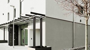 Een modern gebouw met een strakke gevel, een groene deur en een kleine boom op de voorgrond.