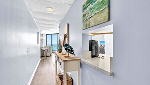 Un espace de bureau moderne avec un long couloir, un comptoir d’accueil en bois, un tableau représentant des oiseaux et une vue sur l’extérieur.