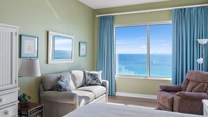 Une chambre avec une grande fenêtre, un canapé, un fauteuil inclinable et un lit.