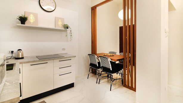 Una cocina moderna con estufa integrada, armarios blancos y un comedor con mesa de madera y sillas blanco y negro.