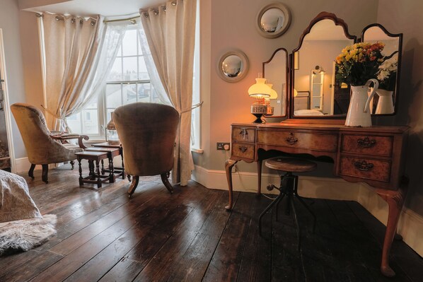A room with a wooden floor, a vintage chair, a wooden dresser with drawers, a mirror, and a lamp.
