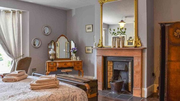 Ein traditionell eingerichtetes Schlafzimmer mit Bett, Schminktisch, Spiegel und Kamin.