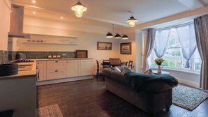 Eine moderne Küche mit weißen Schränken, ein Essbereich mit Tisch und Stühlen sowie ein gemütliches Wohnzimmer mit einer Couch und einem großen Fenster mit Vorhängen.