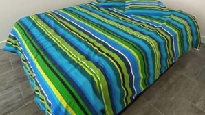 A bed with a striped bedspread in a room with plain walls and a tiled floor.