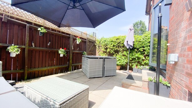 Ein Patio mit Gartenmöbeln, einem großen Sonnenschirm und Topfpflanzen.