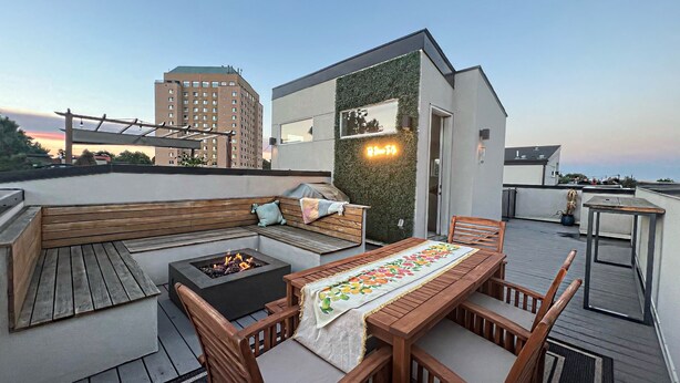 Une terrasse sur le toit avec un banc en bois, un foyer et une table recouverte d’une nappe à motifs floraux.