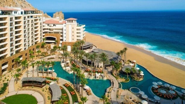 Een resort met meerdere zwembaden, een strand en een bergachtige achtergrond.