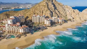 Een hotel aan de kust met meerdere gebouwen, een strand en een berg op de achtergrond.