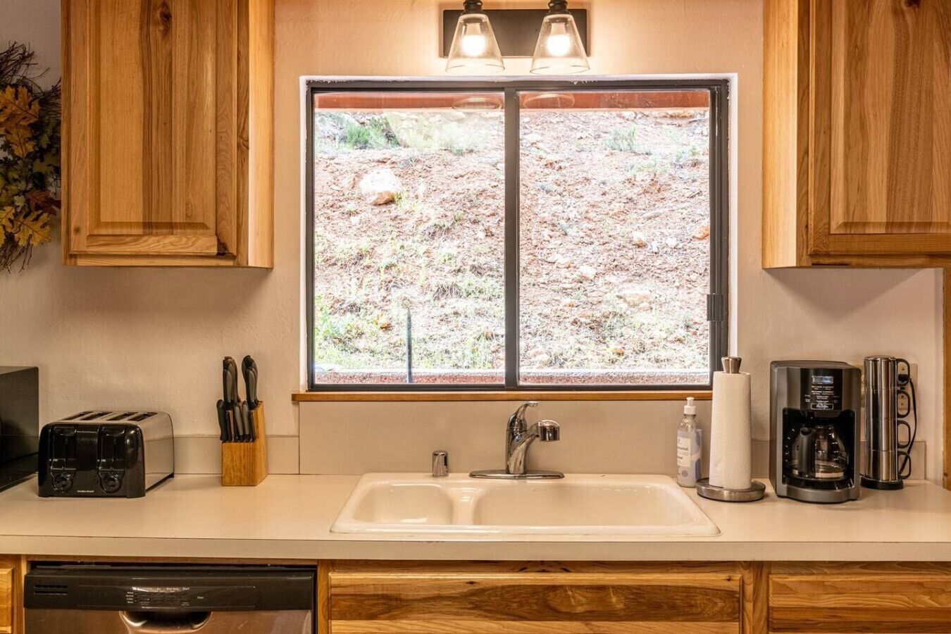 A kitchen with a double sink, a toaster, a coffee maker, and a window with a view of a rocky landscape.