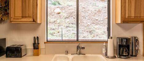 Una cocina con un lavaplatos doble, un tostador, una cafetera y una ventana con vista a un paisaje rocoso.