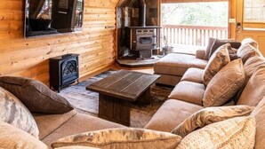 Interior acolhedor de uma cabana com decoração em madeira, lareira, sofá e televisão.