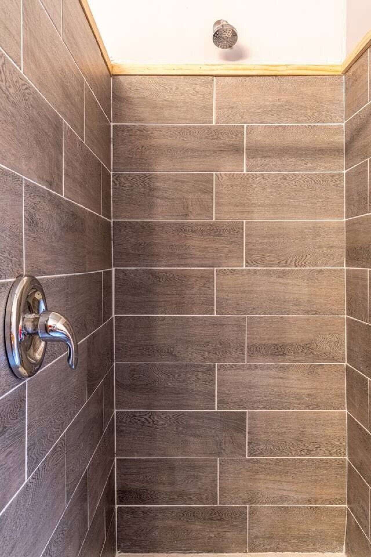 Un espace douche avec des carreaux à motifs de bois foncé et une pomme de douche chromée.