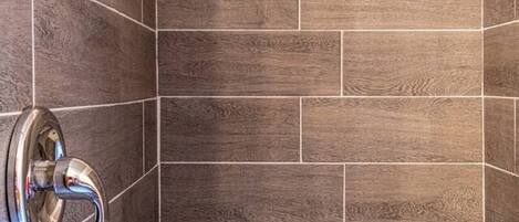 Un espace douche avec des carreaux à motifs de bois foncé et une pomme de douche chromée.