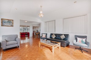 A spacious living room with hardwood flooring, a chandelier, and a dining area with a table and chairs.