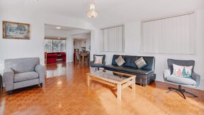 A spacious living room with a wooden floor, a grey sofa, a red sofa, and a grey armchair. There is a wooden coffee table in the center.