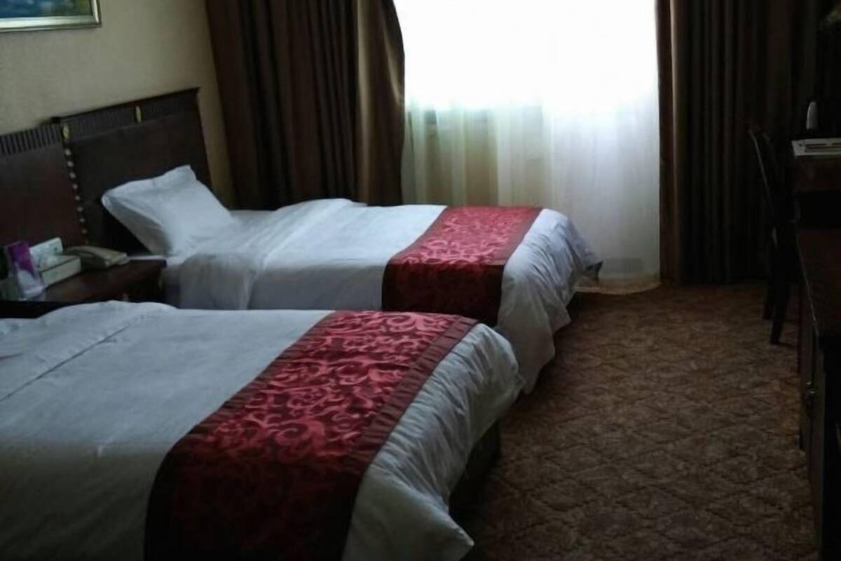 Two beds with red and white bedding, a wooden headboard, a desk, and a chair in a hotel room.