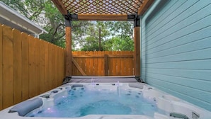 A hot tub with a wooden deck and a pergola overhead.