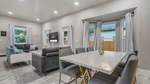 A modern living room with a white dining table, grey sofas, and a TV.