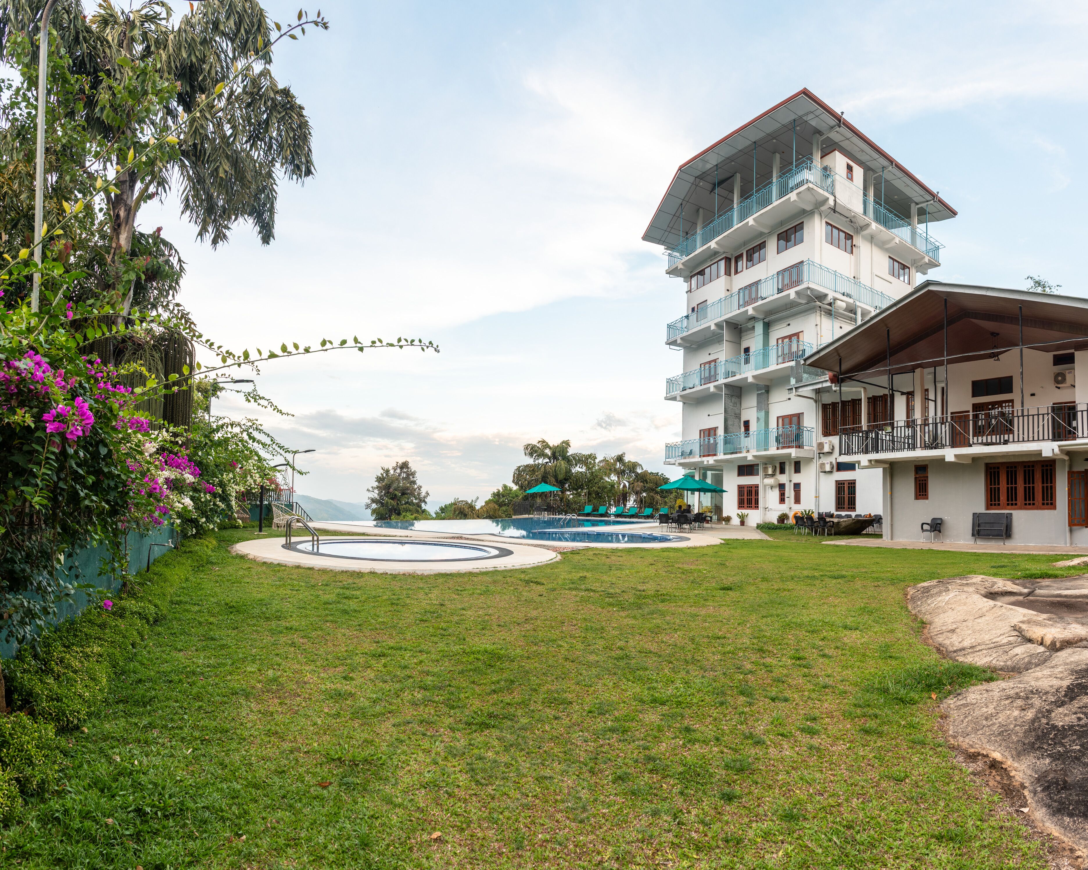 A hotel with a swimming pool, outdoor seating, and a large building with multiple balconies.