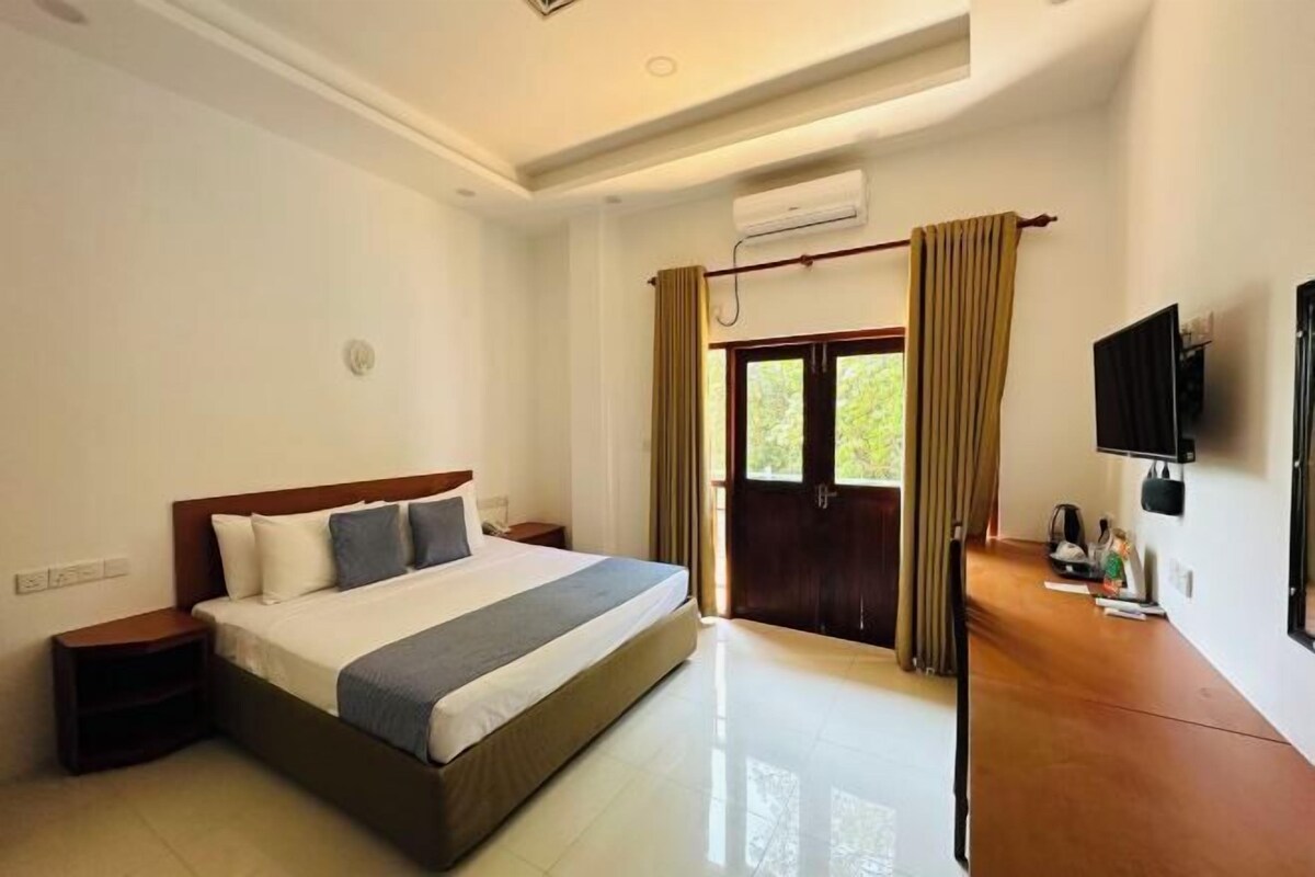 Quarto de hotel com uma cama grande, televisão de tela plana, escrivaninha e janela com cortinas.
