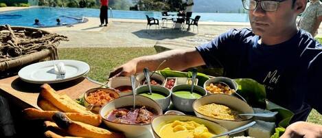 A dining table with various dishes, a pool, and a mountainous backdrop.