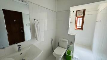 A small, clean bathroom with white tiles, a white sink, a toilet, and a green trash bin.
