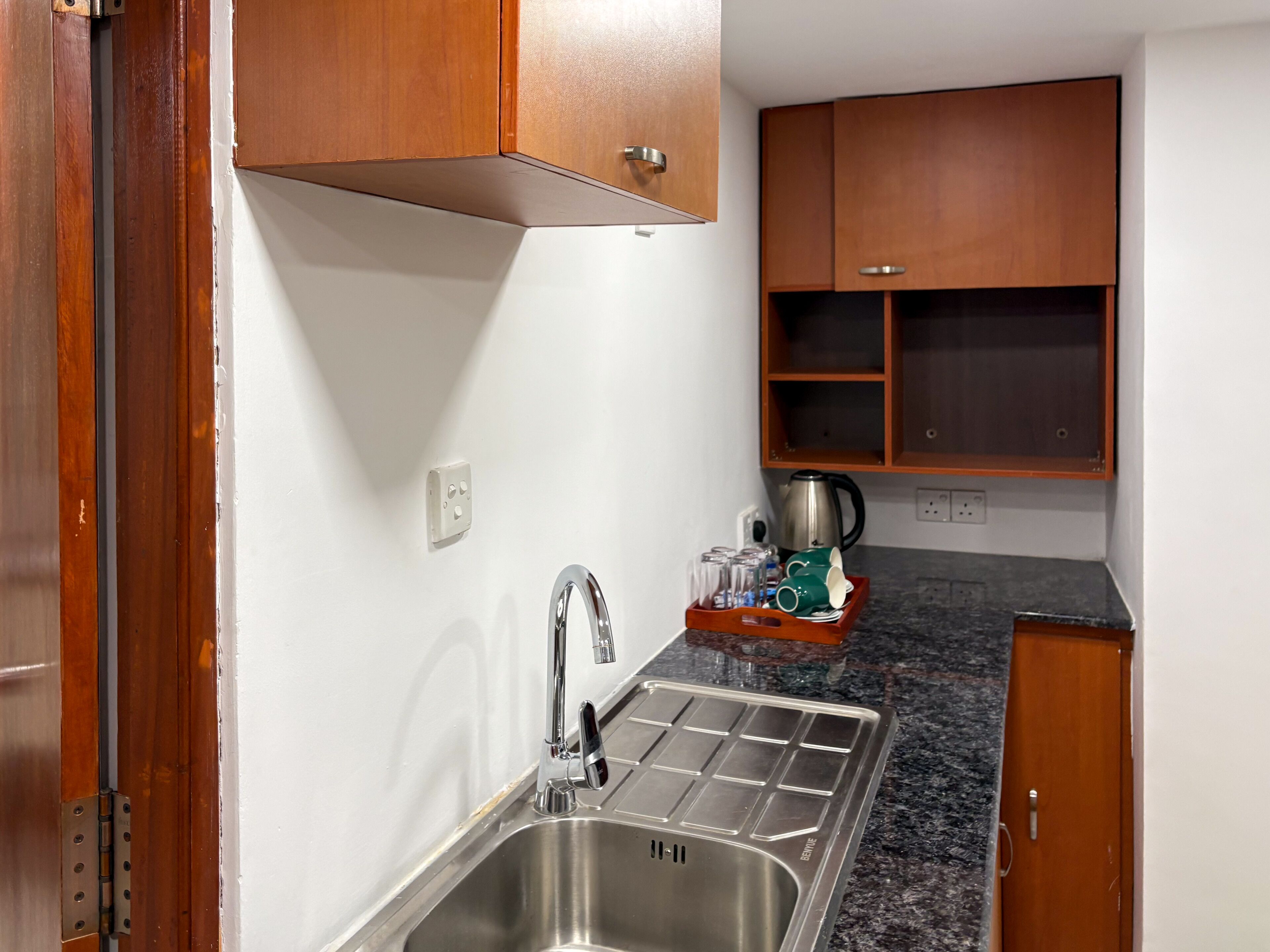 A kitchen with a stainless steel sink, wooden cabinets, a coffee maker, and a tray with glasses and cups.
