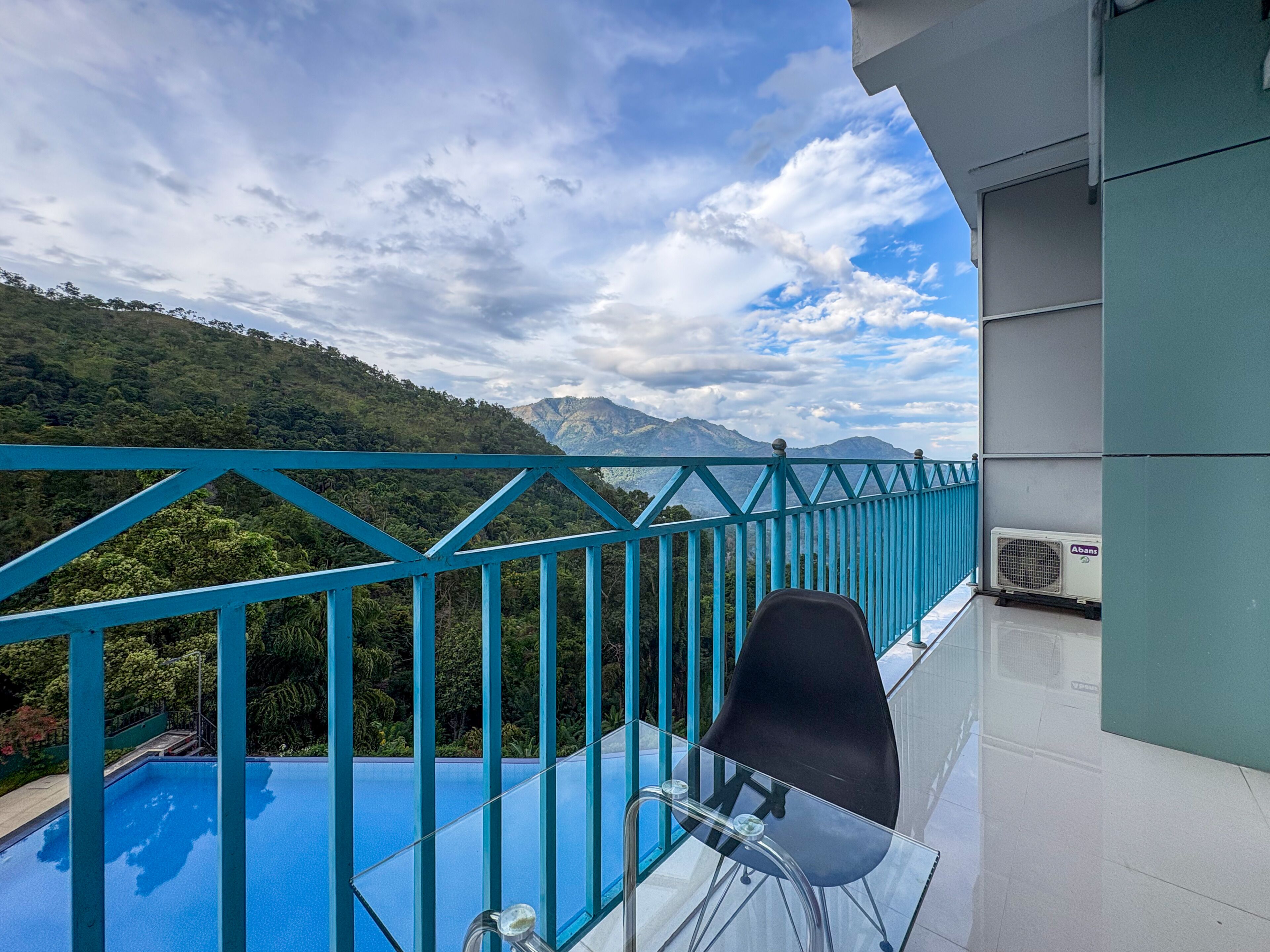 A balcony with a glass table and chair, overlooking a mountainous landscape.
