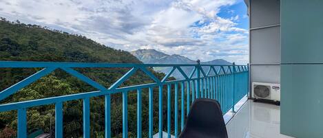 A balcony with a glass table and chair, overlooking a mountainous landscape.
