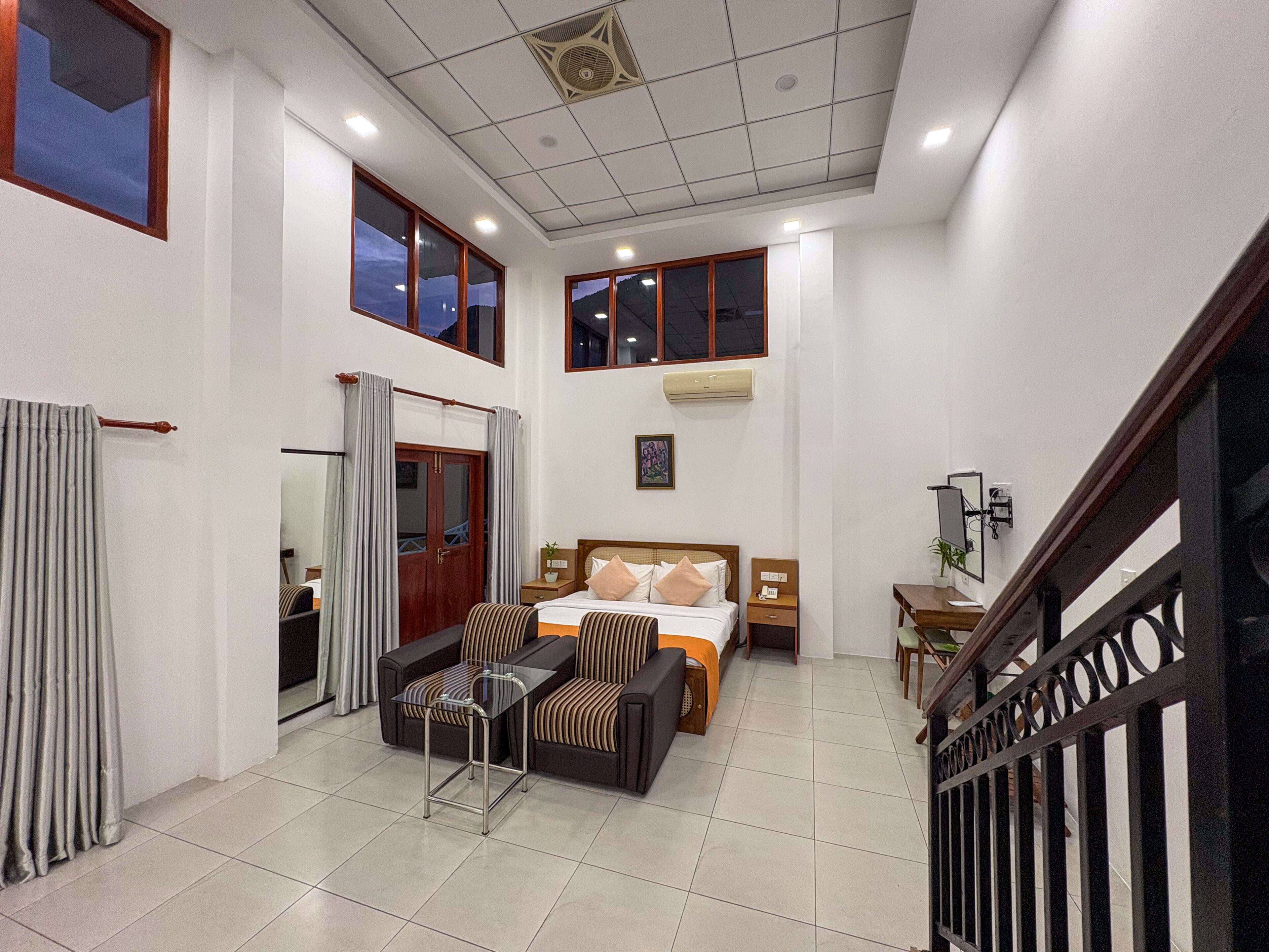 Una habitación de hotel con cama, sofá, mesita, espejo y una escalera.