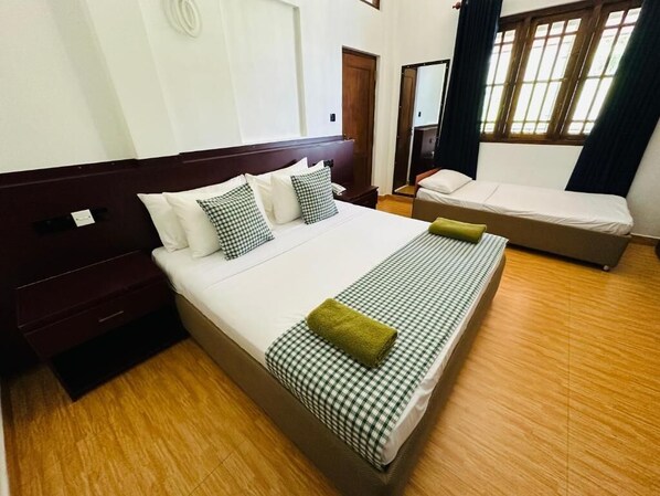 Habitación de hotel con una cama grande, una cama individual, piso de madera, espejo y ventana con cortinas.