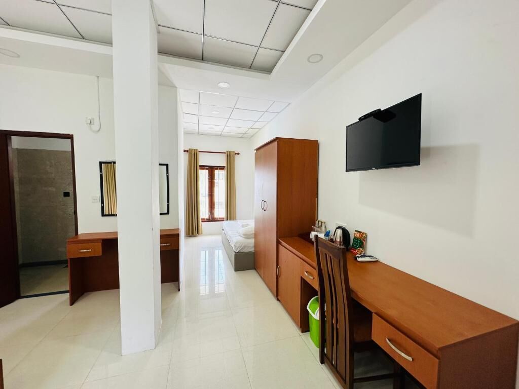 A hotel room with a bed, a desk, a television, and a trash bin.