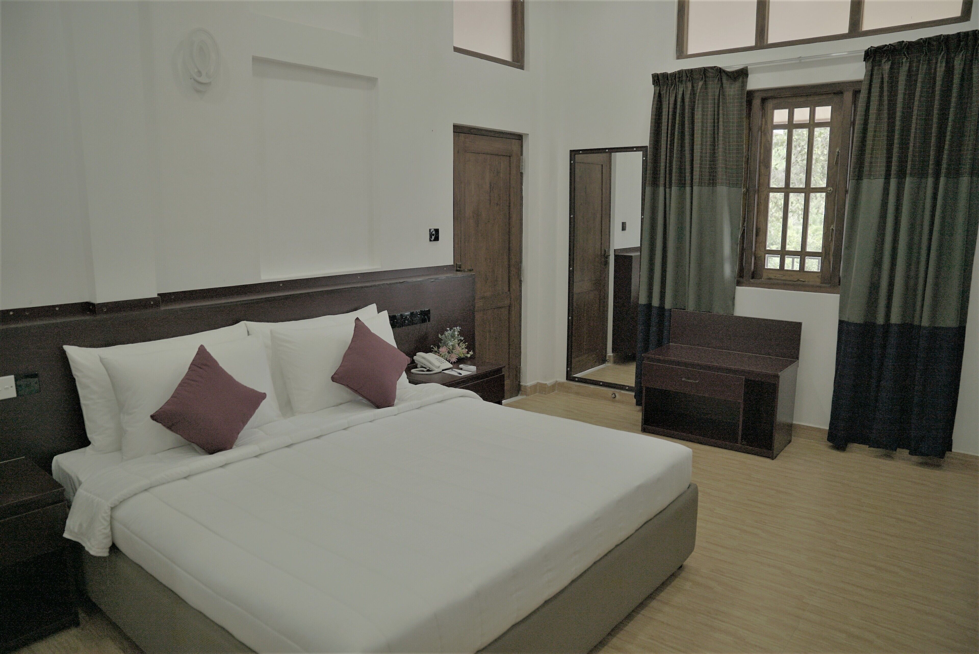 Habitación de hotel con una cama grande, una mesita de noche, un escritorio y una ventana con cortinas.