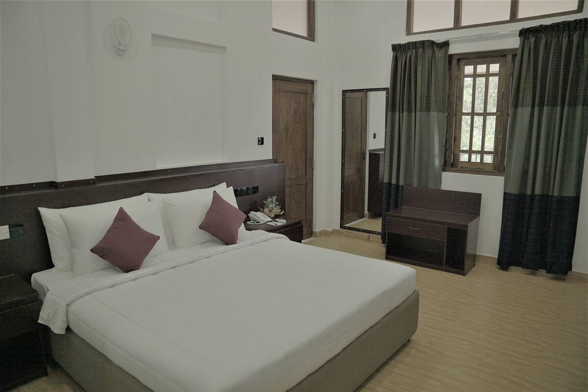 A hotel room with a large bed, a bedside table, a nightstand, a desk, and a window with curtains.
