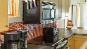 Uma cozinha com micro-ondas, torradeira, cafeteira e facas penduradas acima da bancada.