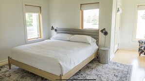 A bedroom with a large bed, two bedside lamps, a rug, and a window with a view of trees.