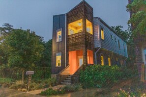 Una casa moderna de dos pisos con fachada oscura, ventanas amplias y una escalera que conduce a la entrada.