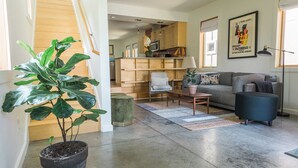 A spacious living area with a large plant, a sofa, a coffee table, and a bookshelf.