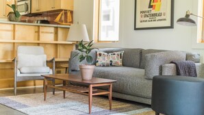 A cozy living room with a grey sofa, a wooden coffee table, a white armchair, and a potted plant.